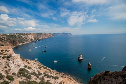 Two rocks stick out of the water in the middle of the turquoise sea. Scenic ocean view. Speed boat sails on the sea. High quality photo.