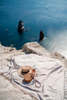 A picnic blanket, champagne, two glasses, a hat and a straw purse. Top on the mountain against the background of the sea and rocks in the sea