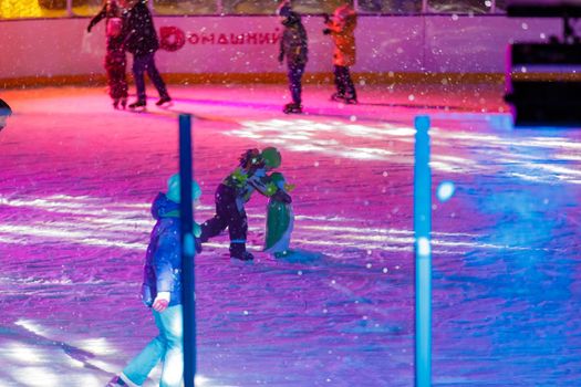 People skate in the evening on a lighted ice rink. A blizzard is raging and snow is falling. Zelenograd, Russia 28.01.2022.