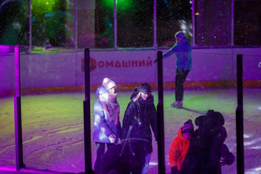 People skate in the evening on a lighted ice rink. A blizzard is raging and snow is falling. Zelenograd, Russia 28.01.2022.