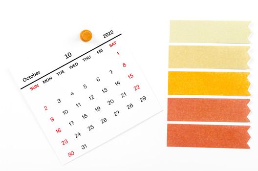 The October 2022 calendar with wooden push pin and blank adhesive note paper on white background.