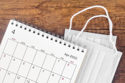 April 2022 desk calendar with surgical mask medical on wooden background.