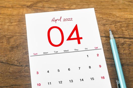 The April 2022 calendar with pen on wooden table.