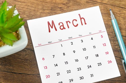 The March 2022 calendar and pen on wooden background.
