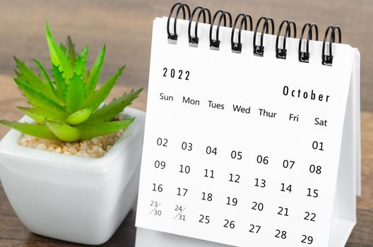 The October 2022 desk calendar with plant pot on wooden table.