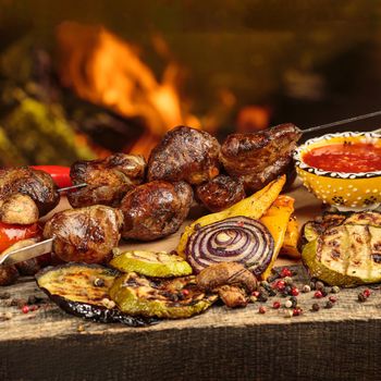 Shashlik or shish kebab prepared on barbecue grill over hot charcoal with grilled vegetables. Grilled pieces of pork meat on metal skewers.