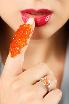 Close-up girl with red caviar on her finger.