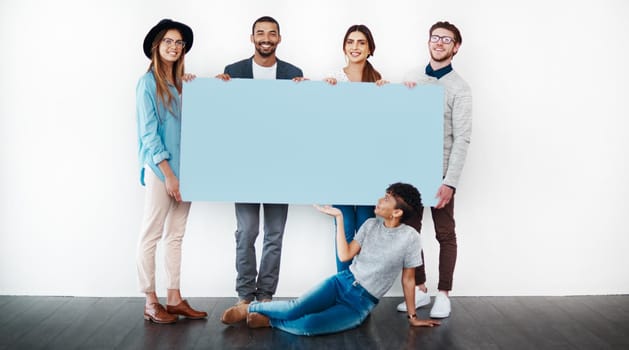 Studio shot of a group of young people holding a blank placard against a white background.