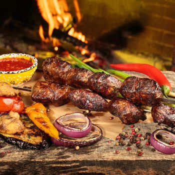 Shashlik or shish kebab prepared on barbecue grill over hot charcoal with grilled vegetables. Grilled pieces of pork meat on metal skewers.