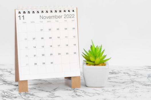 The November 2022 desk calendar with plant on marble table.