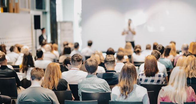 Speaker giving a talk in conference hall at business event. Rear view of unrecognizable people in audience at the conference hall. Business and entrepreneurship concept.