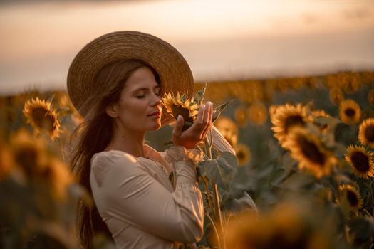 Beautiful young woman in a hat enjoying nature on a field of sunflowers at sunset. Summer. Attractive brunette with long healthy hair