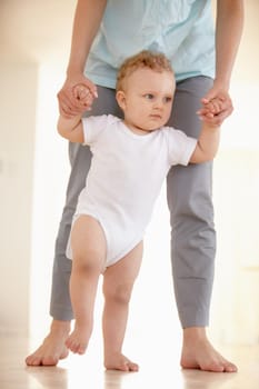 Cropped image of the legs of a baby walking with a parent supporting from behind.