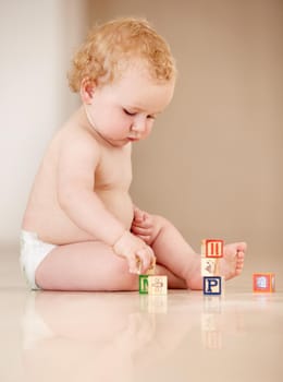 Cute little baby sitting on the ground and playing with some alphabet blocks.