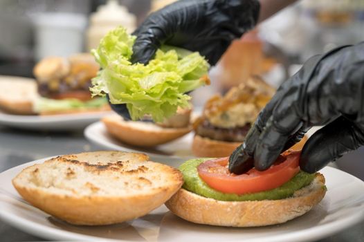 Chef cooking burger, close-up, making sandwich, fast food concept, recipe of preparing homemade hamburger with vegetables. High quality photography.