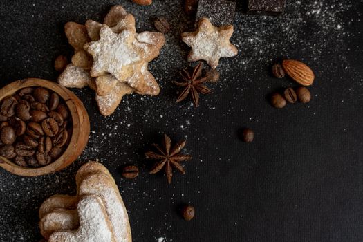 black background with homemade cakes, fragrant cookies. Cookies in the form of hearts, stars, coffee beans, spices, almonds close-up. Full size