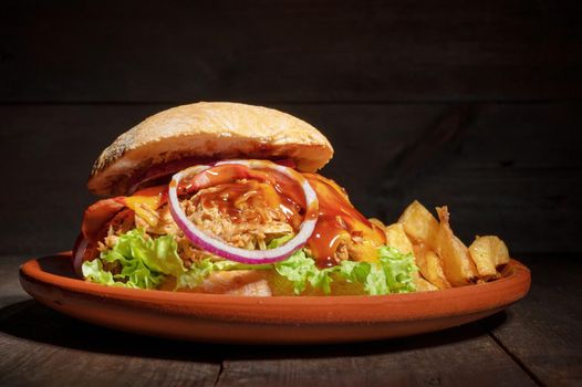 Pulled Pork Burger with lettuce, cheese, onion and barbecue Sauce, served on a rustic plate on wooden table. High quality photography.