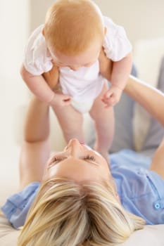 An adorable baby girl being lifted into the air by her mother.