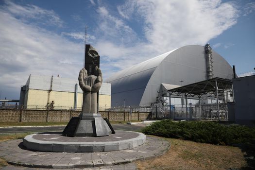 Monument to the casualties of the Chernobyl disaster in front of the New Safe Confinement in Chernobyl Exclusion Zone, Chernobyl, Ukraine