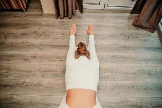 Adult athletic woman, in white bodysuit, performing fascia exercises on the floor - caucasian woman using a massage foam roller - a tool to relieve tension in the back and relieve muscle pain - the concept of physiotherapy and stretching training.