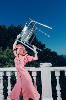 woman with pink hair in glasses with a chair in her hands on the balcony. High quality photo