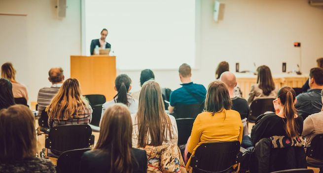 Speaker Giving a Talk at Business Meeting. Audience in the conference hall. Business and Entrepreneurship. Focus on unrecognizable people from rear.