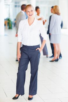 Full length of attractive female executive smiling with business people discussing in background.