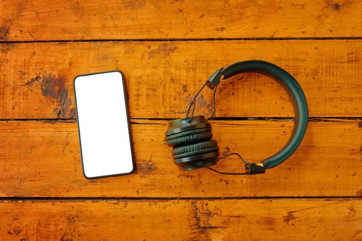 Headphones and smartphone on wooden table. Top view on mobile phone with empty screen. Instagram blogging. Copy space for text.