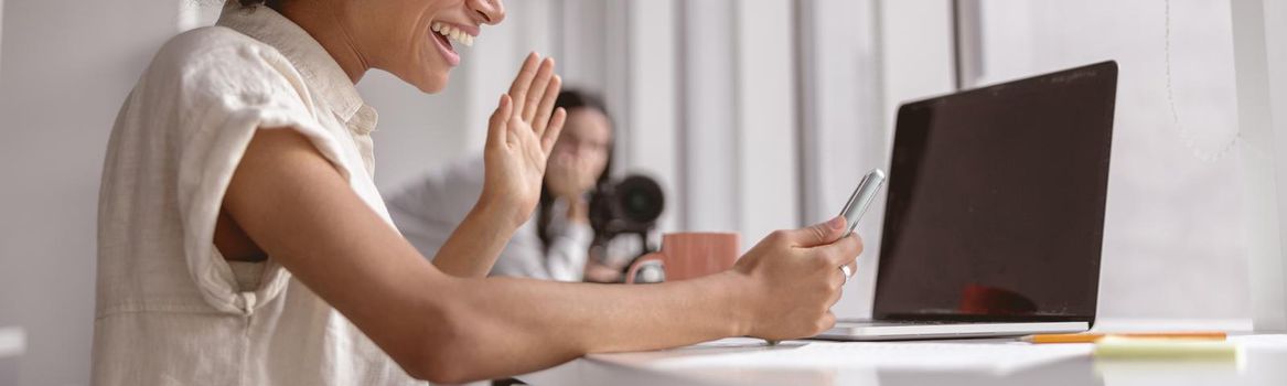 Smiling pretty multiethnic lady waving hand while making a video call on a mobile phone in the office