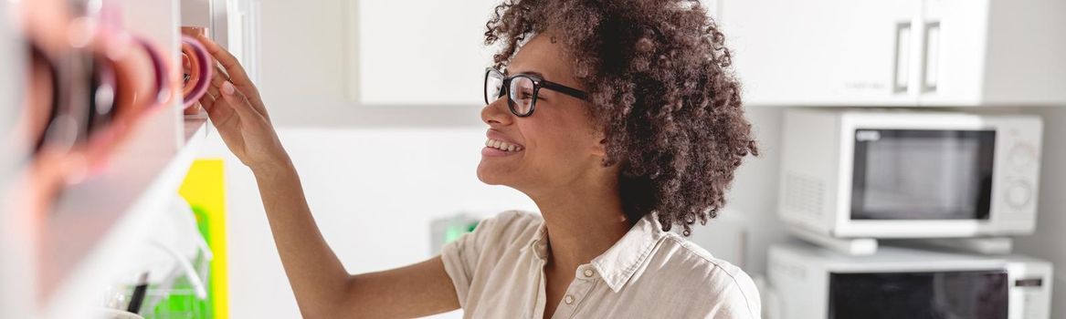 Smiling young woman holding smartphone while going to make coffee on office kitchen