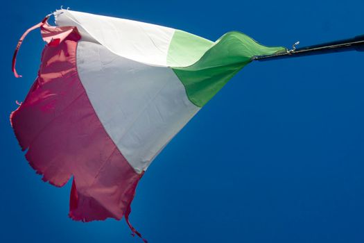 The Italian tricolor flag worn and torn by the wind in a blue sky 
