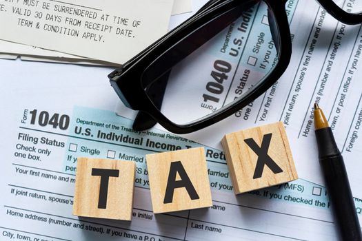 Text on Alphabet wooden block cube with Tax forms 1040. U.S Individual Income Tax Return on a desk. Business and tax concept. Time to pay tax in year.