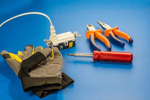 Gloves, electric socket with electrician's tools lie against a blue background