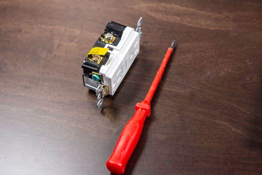 A tested electrical outlet lies on the table before being installed in a junction box on the wall.