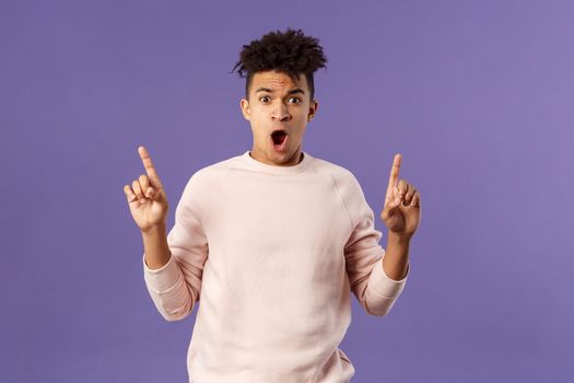 Portrait of shocked, speechless young hispanic man with dreads reacting to overwhelming shook news, gasping, drop jaw and staring concerned as pointing up at something astounding.