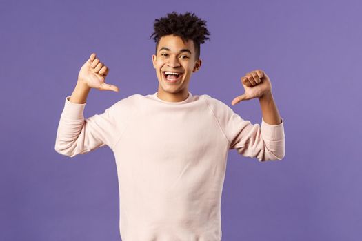 Portrait of confident young upbeat man, smiling bragging, being boastful about own accomplishments, indicate himself with proud rejoicing face, standing purple background.