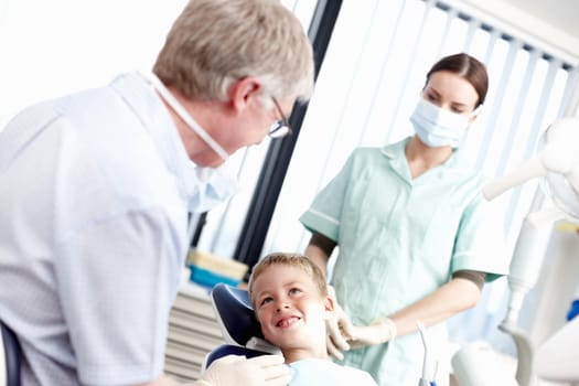 Portrait of young boy smiling at dentist with assistant in office.
