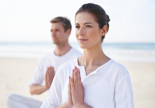 A young couple practising yoga on the beach.