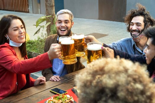 Group of multiracial friends toast with beers in a restaurant. Face mask on chin. Friendship concept.