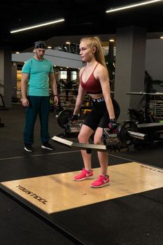 RUSSIA, MOSCOW - FEB 11, 2022: Instructor and client girl deadlift blonde trap bar personal exercise, from instructor motivation in healthy and personal support, ar lift. Heavy man bodybuilding, muscular