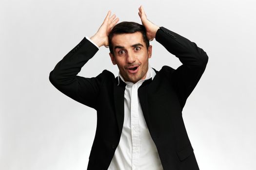 portraits of a man in a black business suit with a surprised expression straightens his hair on a white studio background, copy space. High quality photo