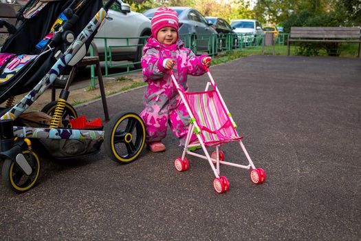 little girl plays walking with toy stroller near real baby stroller like mom