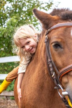 caucasian little girl hugs pony horse and laugh happily