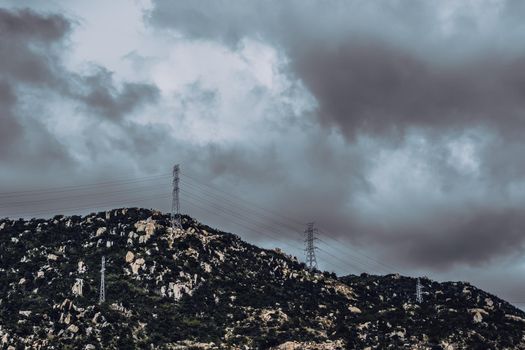 Real nature landscape background. Rocky mountain, cloudy Pale Blue dark stormy sky autumn day, high voltage Electricity power pylons. Cold mood feelings. Problem Difficult obstacles, discomfort.