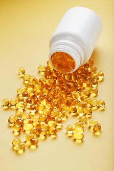 Gold Vitamin D3 capsules poured out of a jar on a yellow background with free space. The most important vitamin in an easily digestible liquid form.