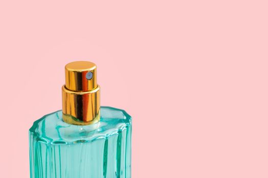 Beautiful modern perfume bottle. Minimalistic style with transparent glass in green colors and golden lid on pink background. photo