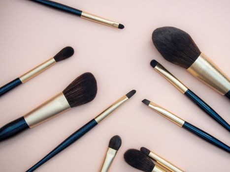 Assortment of female make-up of various face brushes. A set of professional dark blue and golden makeup brushes on a pink background. photo