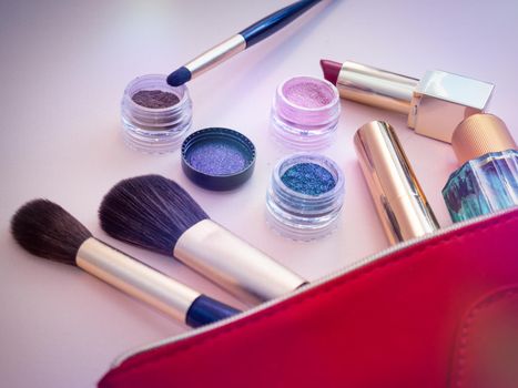 Top view of cosmetics standing out from red cosmetic bag on pink background. Photo