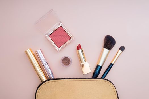 Top view of cosmetics standing out from beige makeup bag on pink background. Photo