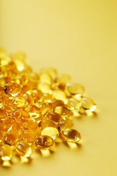 Heap of transparent fish oil capsules on yellow background with free space.